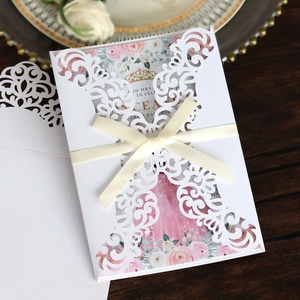 Detail of laser-cut invitation with white bow and pink floral inner card on wooden table