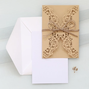 Detail of laser-cut floral kraft paper invitation with rustic twine and white envelope
