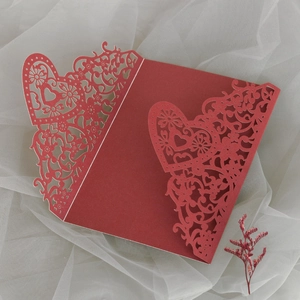Macro detail of wine red laser-cut wedding invitation featuring heart and floral motifs