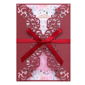Macro detail of laser-cut burgundy invitation with red ribbon and floral Quinceañera card