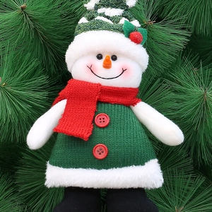Plush Christmas snowman doll with green sweater and red scarf on pine needle background