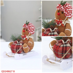 Detail of gingerbread man doll on a white sled with a red plaid gift bag and pine cones