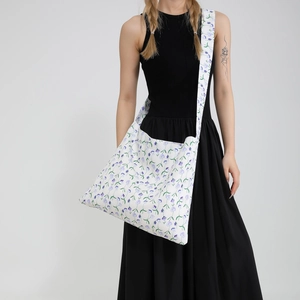 Floral canvas crossbody tote bag with adjustable strap worn by model in a black dress