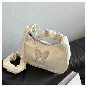 Detail of ruched strap and metallic butterfly charm on creamy off-white shoulder bag