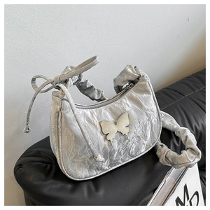 Close-up of a silver pleated shoulder bag with a metallic butterfly charm and bow strap