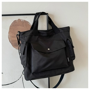 Detail of black nylon tote bag featuring reinforced handles and multi-pocket design