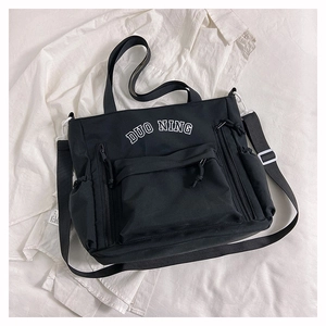 Détail du sac en toile noire avec grande poche zippée et broderie DUO NING sur le devant