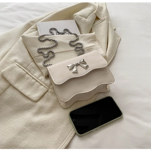 Detail of cream crossbody bag featuring a wavy flap and silver metal bow ornament
