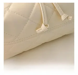 Detail of quilted diamond pattern and side drawstring knot on the beige crossbody bag