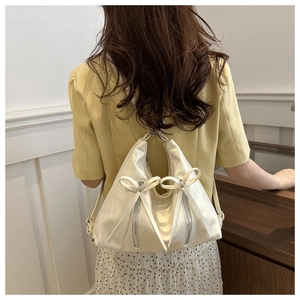 Chic cream bow backpack shown on model wearing yellow blazer and polka dot skirt