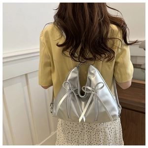 Silver metallic PU backpack with bow detail worn by a model in a cozy indoor setting