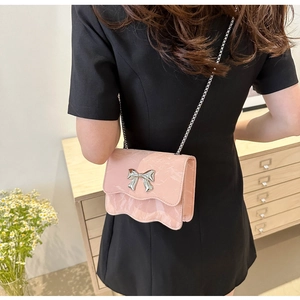Pink crossbody bag with silver bow buckle and chain strap on a model shoulder