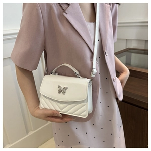 Close-up of white crossbody bag featuring silver butterfly clasp and quilted texture