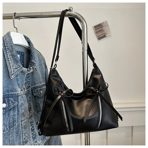 Detail of black tote bag featuring decorative bows and dual silver zippers on faux leather