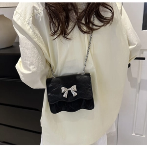 Detail of vintage black leather crossbody bag with silver bow and wavy scalloped edge