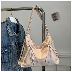 Detailed view of pink hobo bag with bow accents and silver zippers on denim background