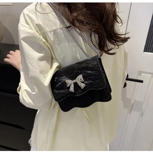 Detail of black pleated shoulder bag featuring a silver bow and delicate chain strap