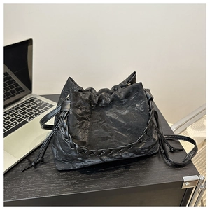 Détail d'un sac seau plissé noir avec chaîne tressée sur un bureau en bois