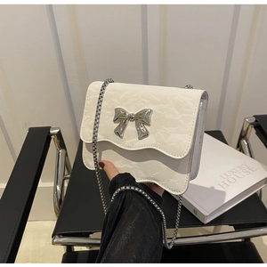 Detail of white crossbody bag featuring a silver bow accent and wavy edge texture