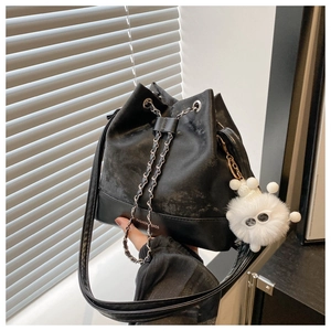 Detail of black drawstring bucket bag featuring a chain strap and plush monster charm