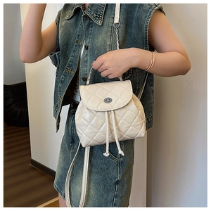 Detail of cream quilted mini backpack showing metal turn-lock and chain strap textures