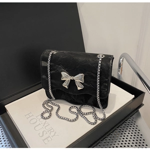 Close-up of black pleated texture crossbody bag with silver metal bow and chain strap
