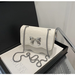 Detail of cream white pleated chain bag featuring a silver metal bow and wavy bottom edge