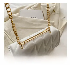 Detail of white quilted faux leather texture and gold chain on small shoulder bag