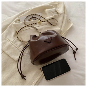 Detail of coffee brown drawstring bucket bag with gold chain strap on beige fabric