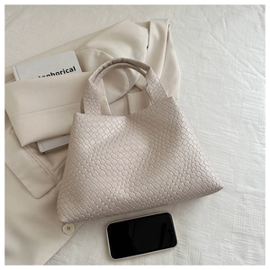 Detailed close-up of cream woven rhombus pattern handbag on textured white fabric
