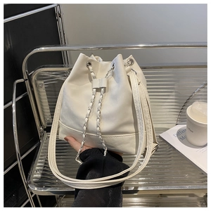 Detailed view of white bucket bag with silver chain drawstring and wide leather strap
