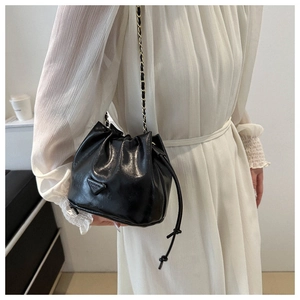 Detail of black glossy bucket bag with golden chain strap on white dress outfit