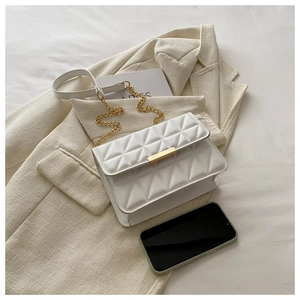 Detail view of white quilted crossbody bag with gold chain strap next to a smartphone
