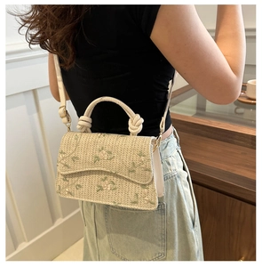 Detail showing woven straw bag with floral embroidery and braided handle in a lifestyle setting