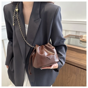 Detail of a dark brown drawstring bucket bag with gold chain strap on a black blazer