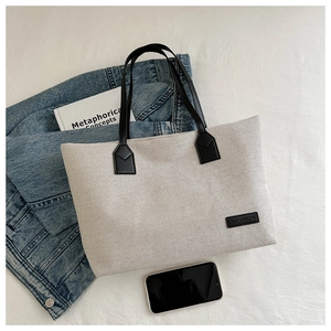 Flat lay of a beige nylon tote bag with black leather handles and daily lifestyle items
