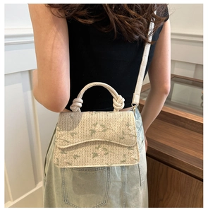 Woven straw crossbody bag with floral embroidery shown on shoulder for size reference