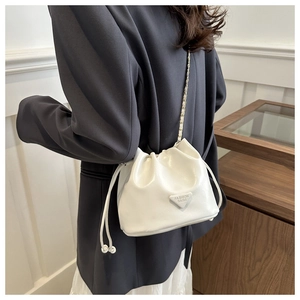 Detail view of white drawstring bucket bag with gold chain strap and metal logo plate