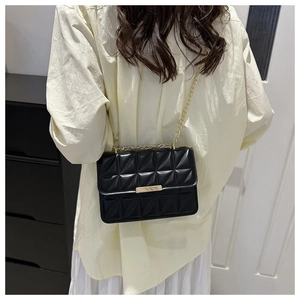 Detailed view of the black quilted crossbody bag with gold chain strap worn on person