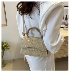 Close-up of woven straw crossbody bag with floral embroidery and white suit background
