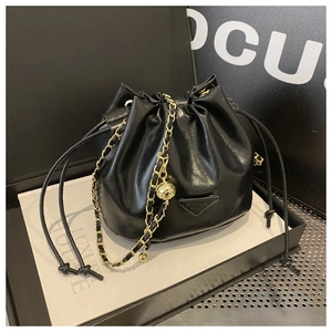 Detail of black drawstring bucket bag with gold chain strap and metal logo plaque