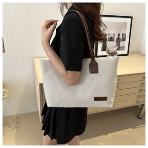 Detail of beige canvas tote bag with brown leather handles and fashion label detail