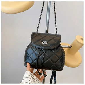 Detail of black quilted leather backpack featuring silver twist lock and chain strap