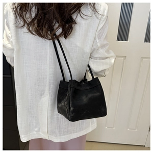 Close-up of minimalist black matte leather bucket bag with slim dual handles on shoulder