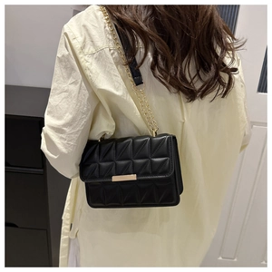 Detail of black quilted shoulder bag with gold chain strap worn by model in casual setting