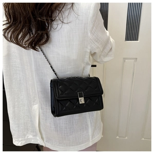 Détail du petit sac bandoulière matelassé noir avec chaîne argentée porté par un mannequin
