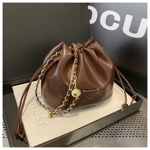 Detail of brown leather drawstring bucket bag with gold chain and metal logo plate
