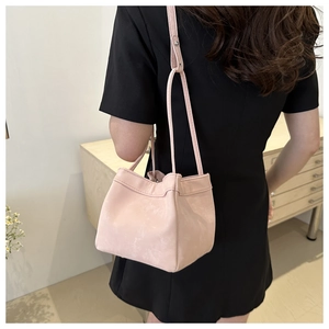 Pink leather bucket bag with adjustable strap shown on a model in a black dress