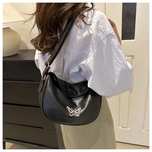 Detail of black faux leather half-moon bag featuring a pink butterfly metal logo buckle