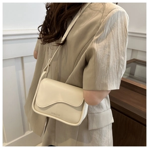 Détail du sac bandoulière crème avec bord ondulé et gaufrage porté par un mannequin